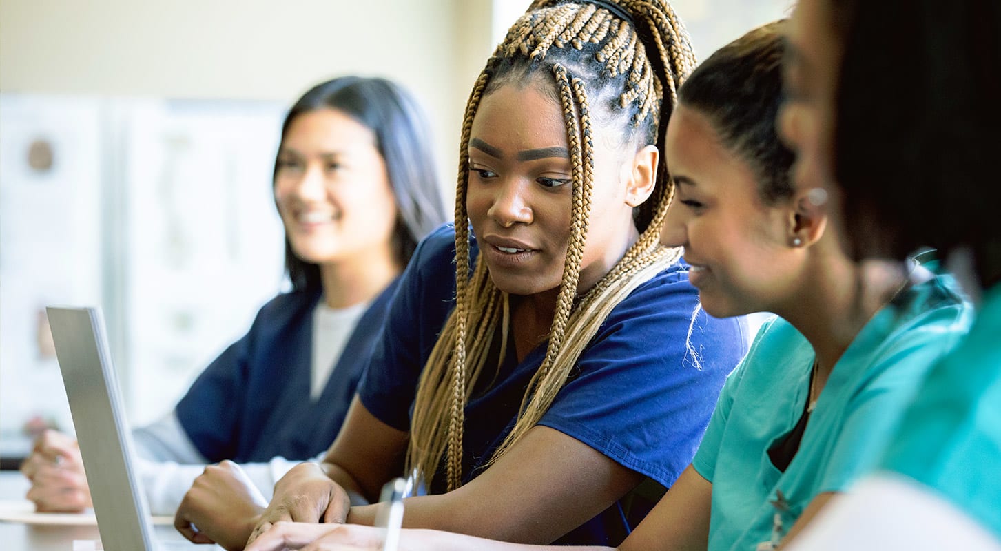 A group of women in scrubs seated around a table, engaged in discussion or collaboration.